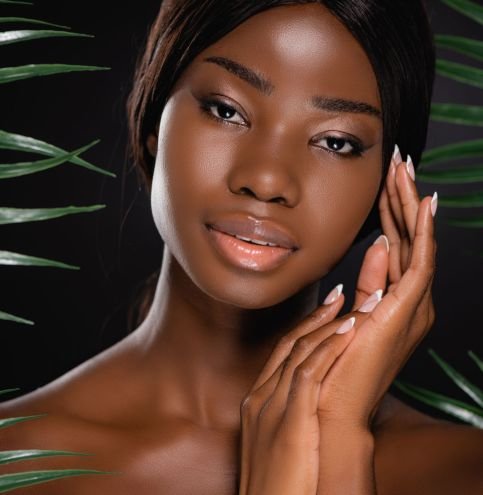 african american naked woman near green palm leaves isolated on black